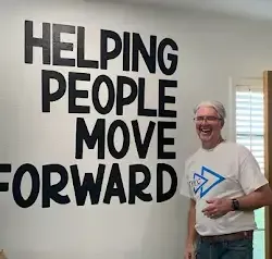 a man is standing in front of a wall that says `` helping people move forward '' .