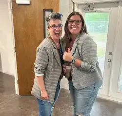 two women are standing next to each other in a room giving a thumbs up .