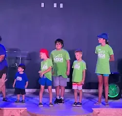 a group of children are standing on a stage wearing green shirts .
