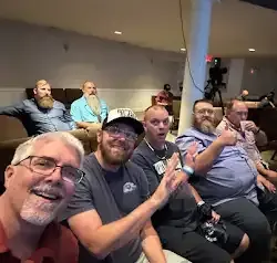 a group of men are sitting in a room taking a selfie .