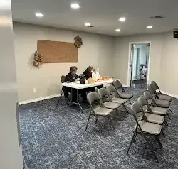 a group of people are sitting at a table in a room with folding chairs .