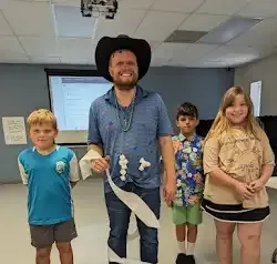 a man in a cowboy hat is standing next to three children in a room .