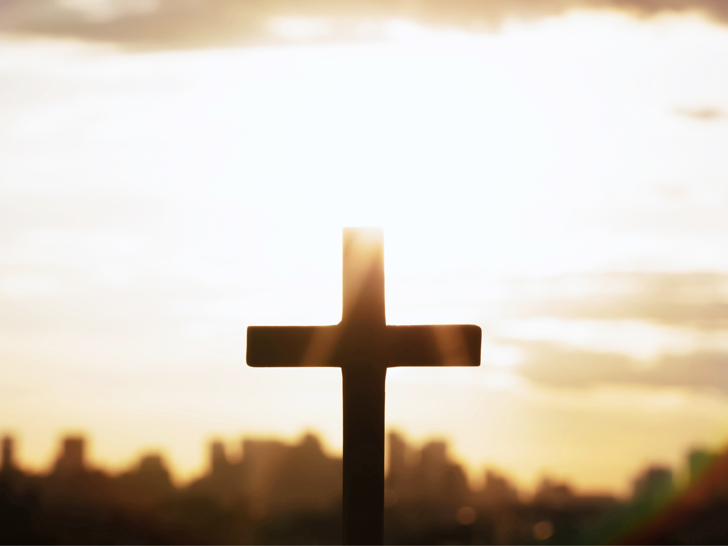 a cross is silhouetted against a sunset sky with a city in the background .
