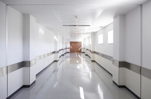 Pasillo de hospital luminoso y vacío con paredes blancas, ventanas y suelo reflectante.