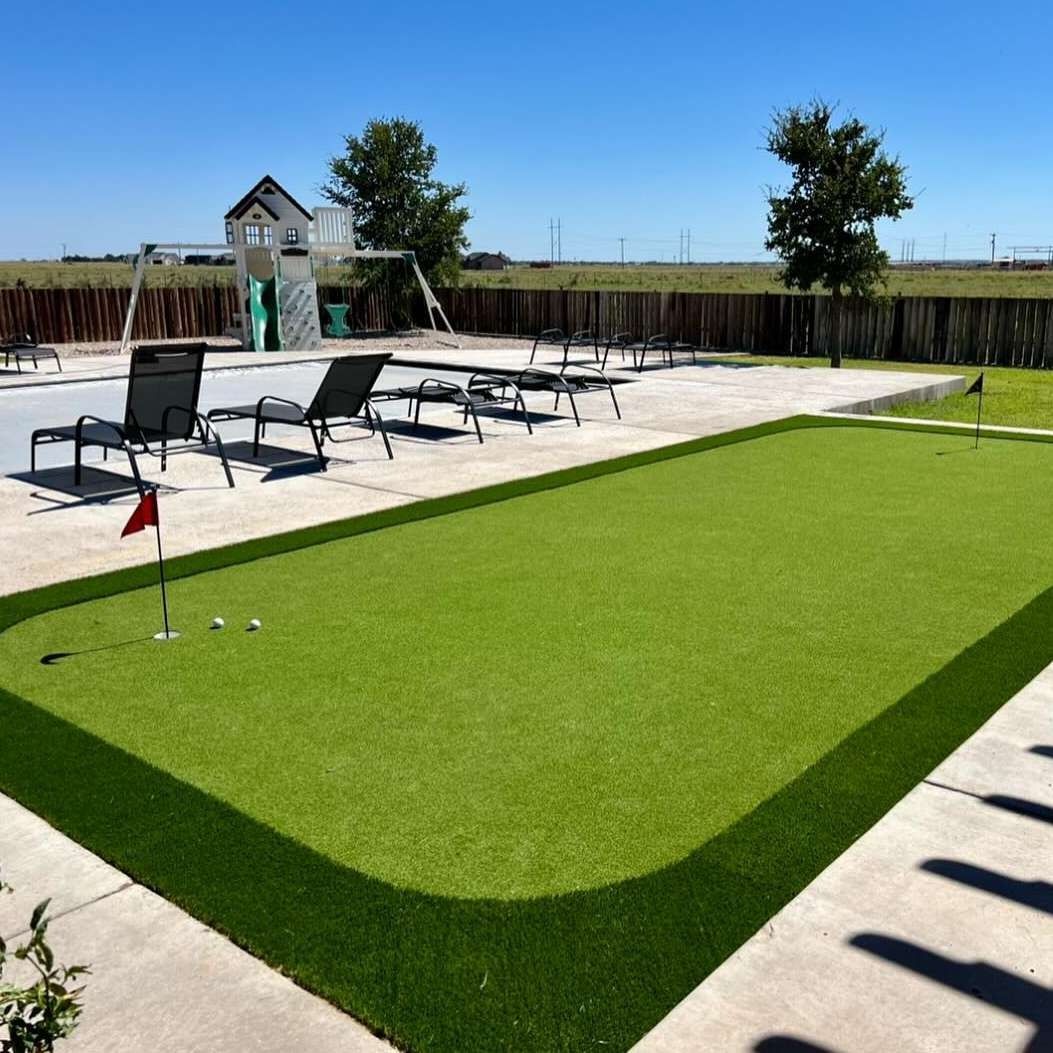 Backyard putting green beside a patio with lounge chairs and a small flagstick