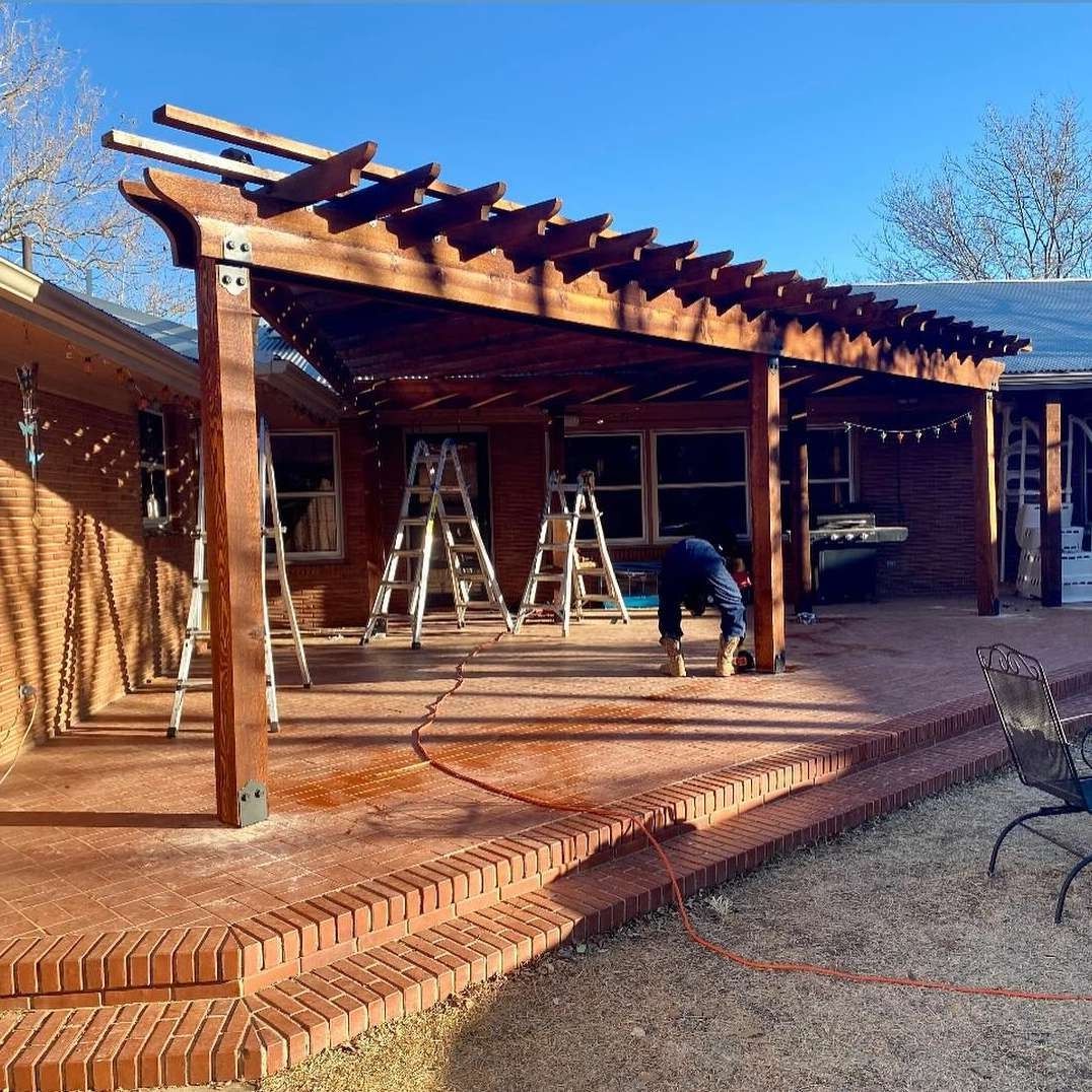Brick patio under wooden pergola with ladders and a person working on the structure.