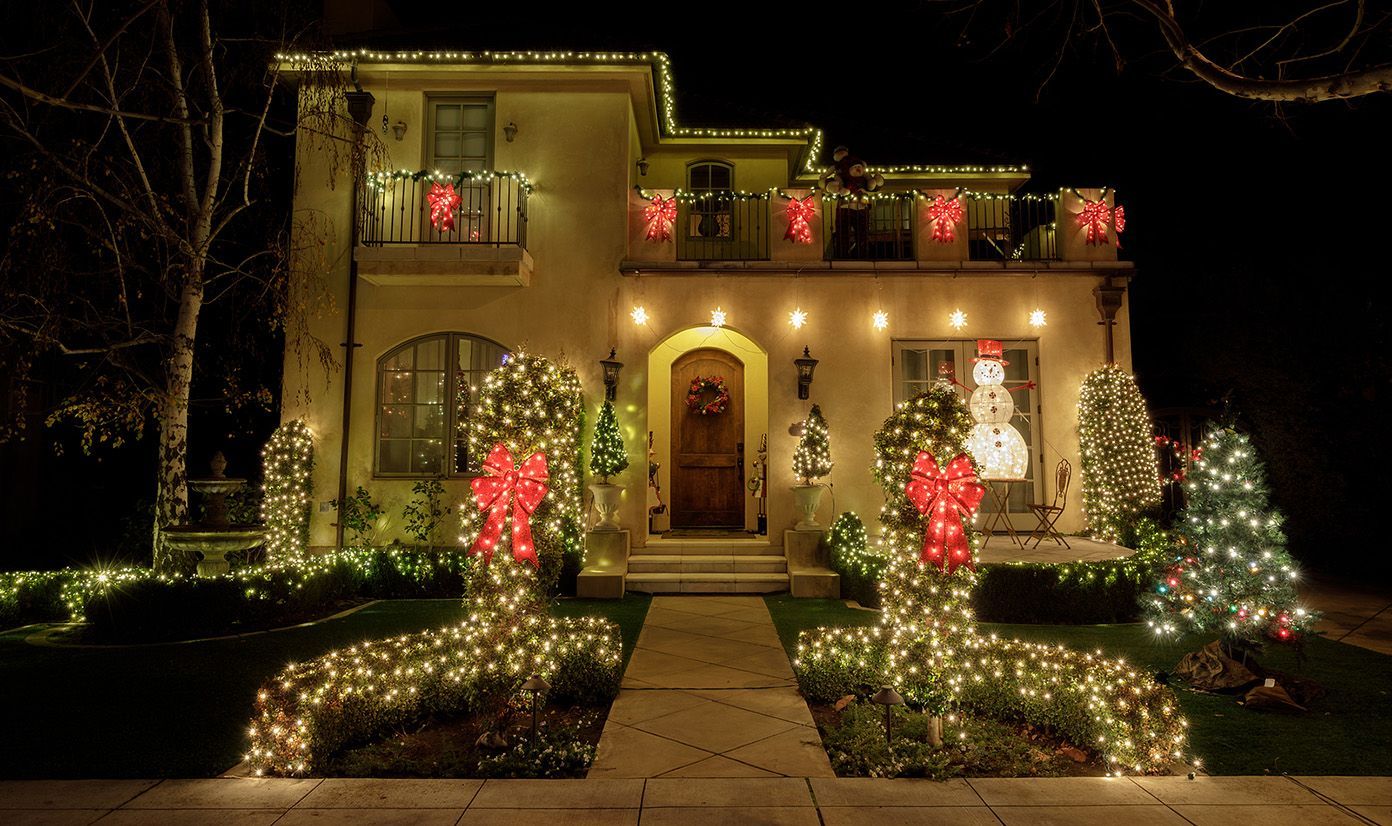 Holiday-lit two-story house at night with red and white Christmas lights and decorated trees in front.