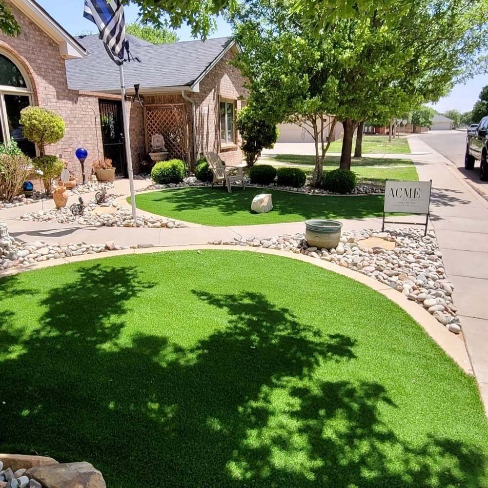 Brick house front yard with bright green lawn, stone edging, and a tree casting shade on a sunny day