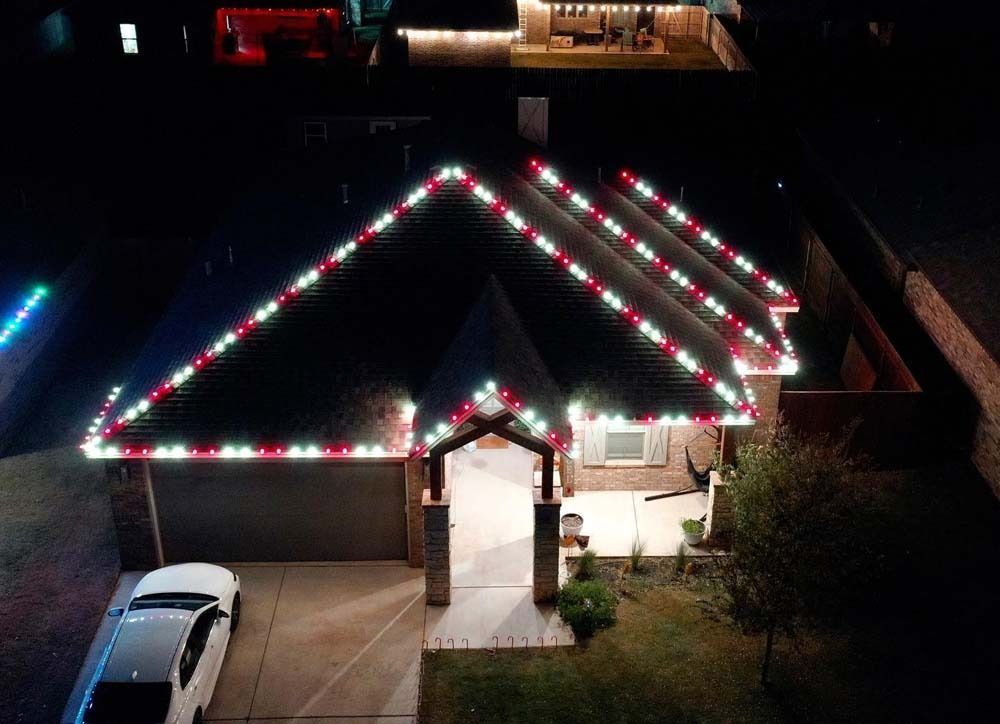 House roof outlined with red, white, and green lights at night, with a lit driveway and walkway