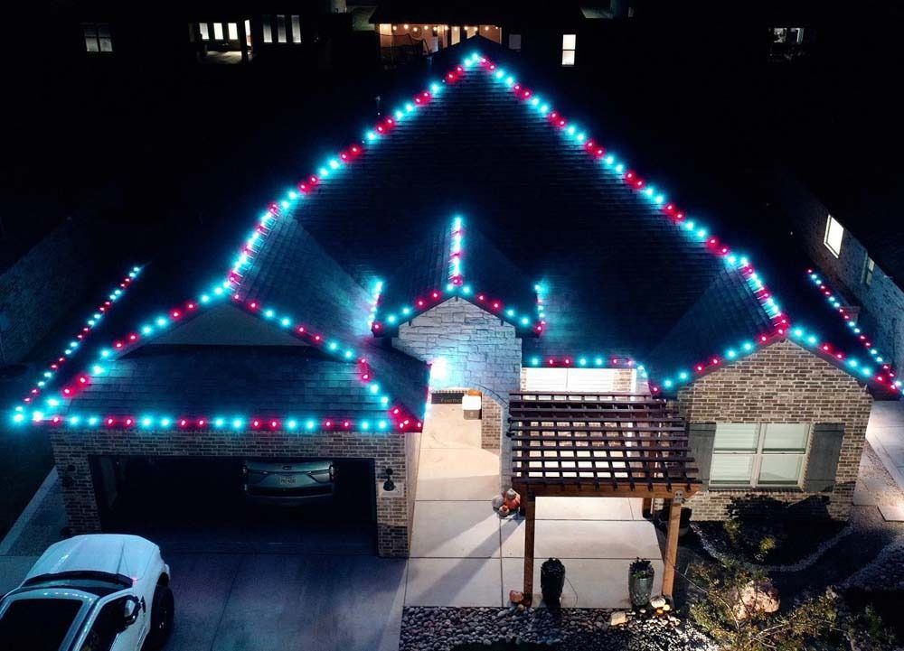 House roof outlined with blue and pink holiday lights at night