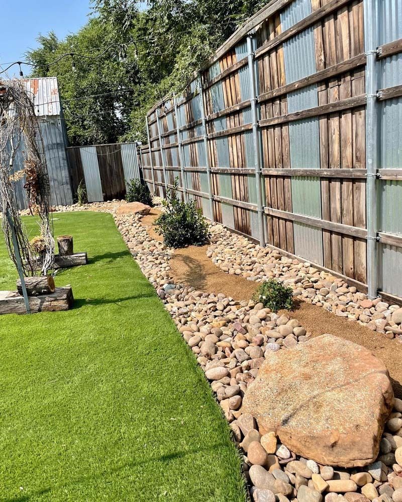Backyard side yard with artificial turf, rock drainage bed, and a weathered wooden fence