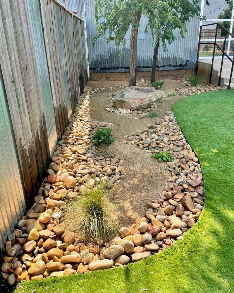 Backyard dry creek bed with river rocks, small plants, a tree, and a lawn edge