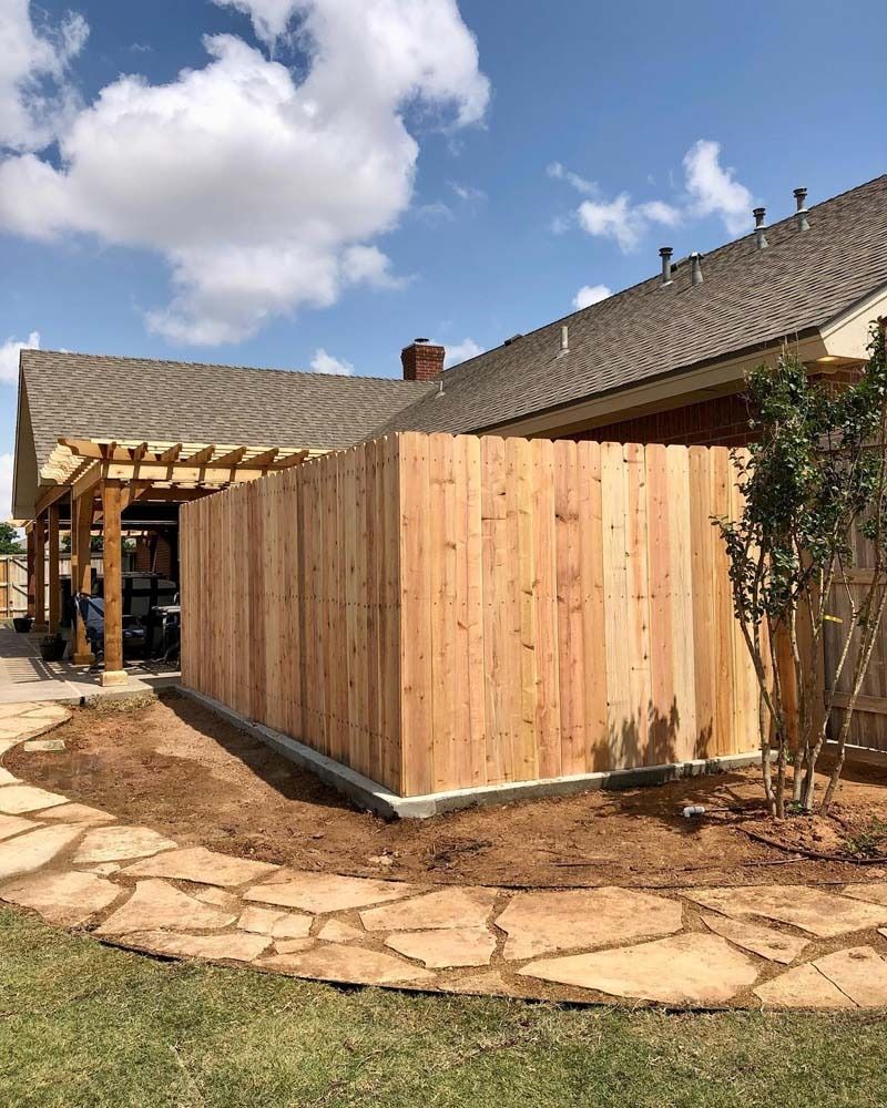 Wooden privacy fence beside a stone patio outside a house under a partly cloudy sky