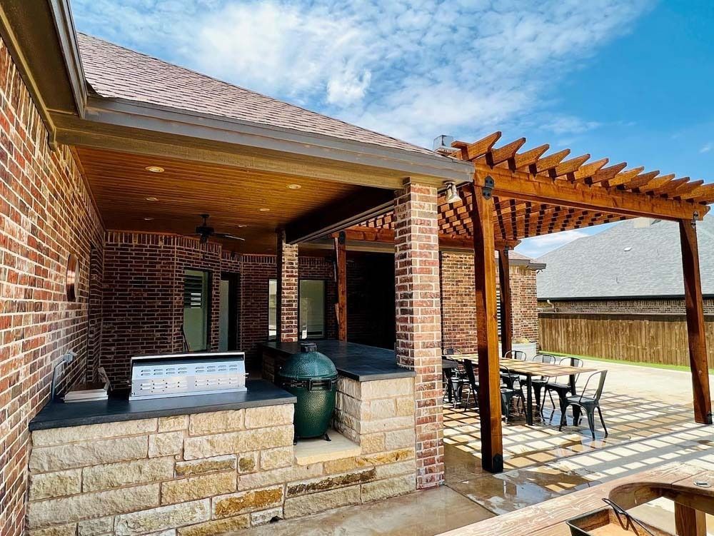 Brick patio with covered outdoor kitchen, grill, and wooden pergola beside a house