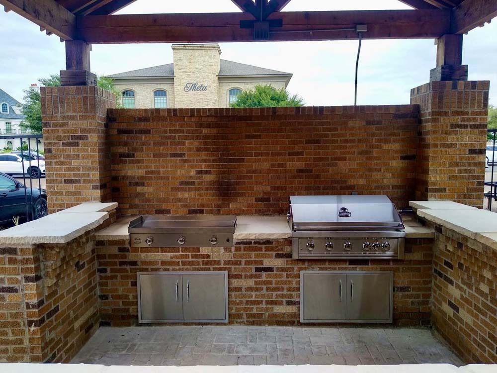 Brick outdoor kitchen with two stainless steel grills under a wooden pavilion