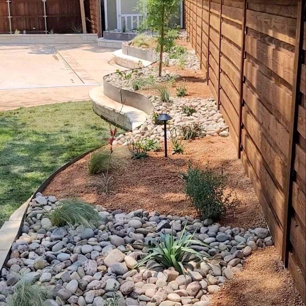 Landscaped side yard with rocks, mulch, small plants, and a wooden fence
