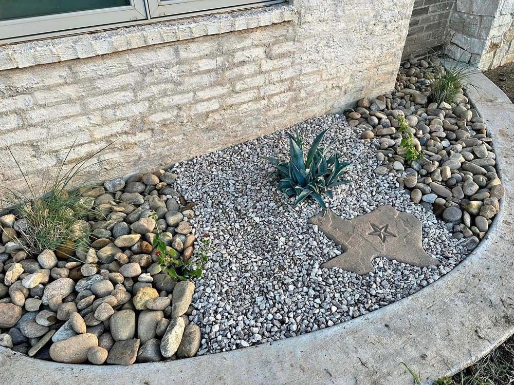 Curved rock garden with pebbles, succulents, and a stone border beside a brick wall