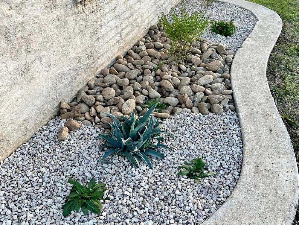 Curved rock garden bed with gravel, decorative stones, and small green succulents beside a wall
