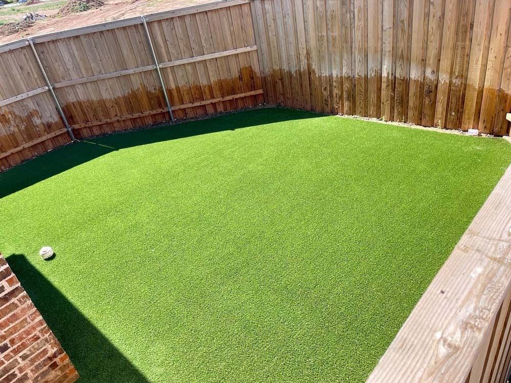Backyard with bright green artificial turf, wooden fence, brick wall, and a small soccer ball in the corner