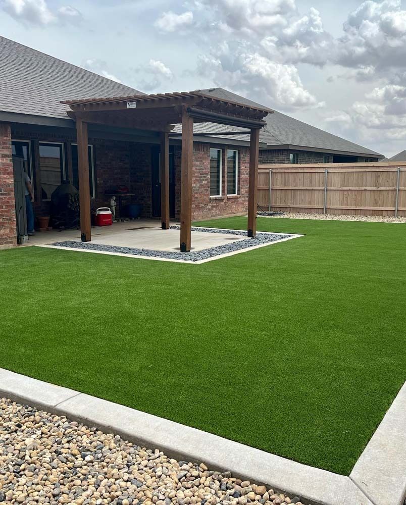 Backyard with bright green lawn, covered patio, brick house, and wooden fence under cloudy sky