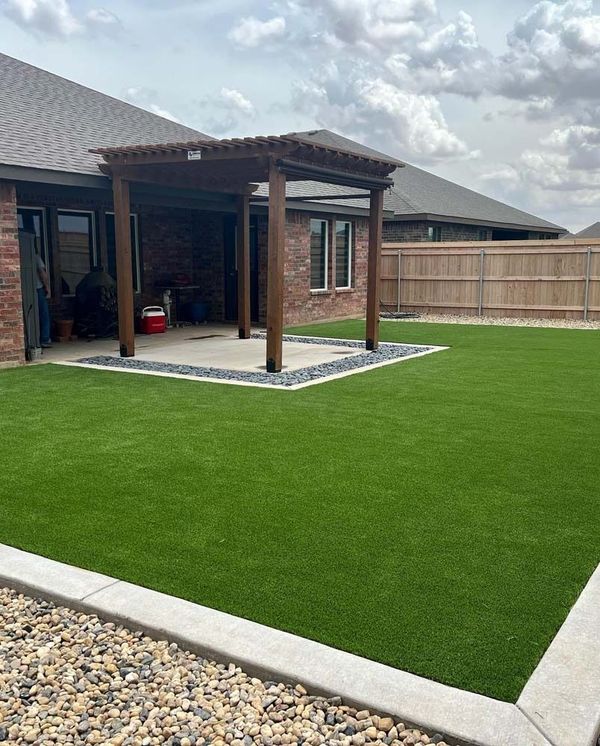 Backyard patio with artificial grass, a covered seating area, and a wooden fence under cloudy sky