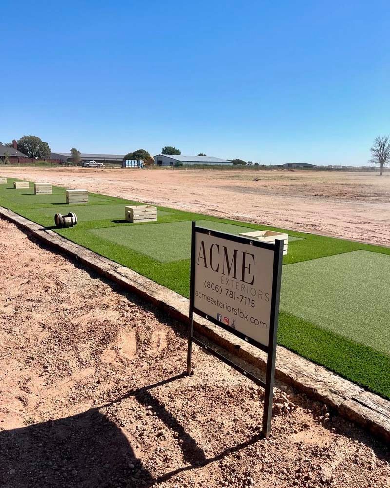 ACME golf course sign beside a green putting area and sandy fairway under a clear blue sky