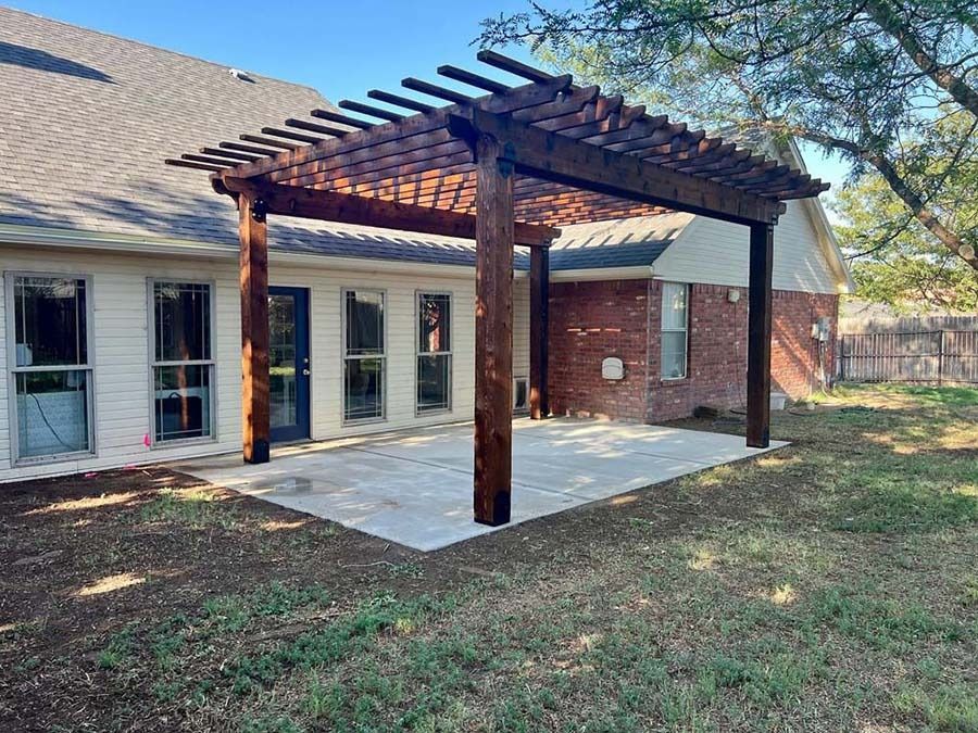 Back patio with wooden pergola over a concrete slab beside a brick-and-siding house