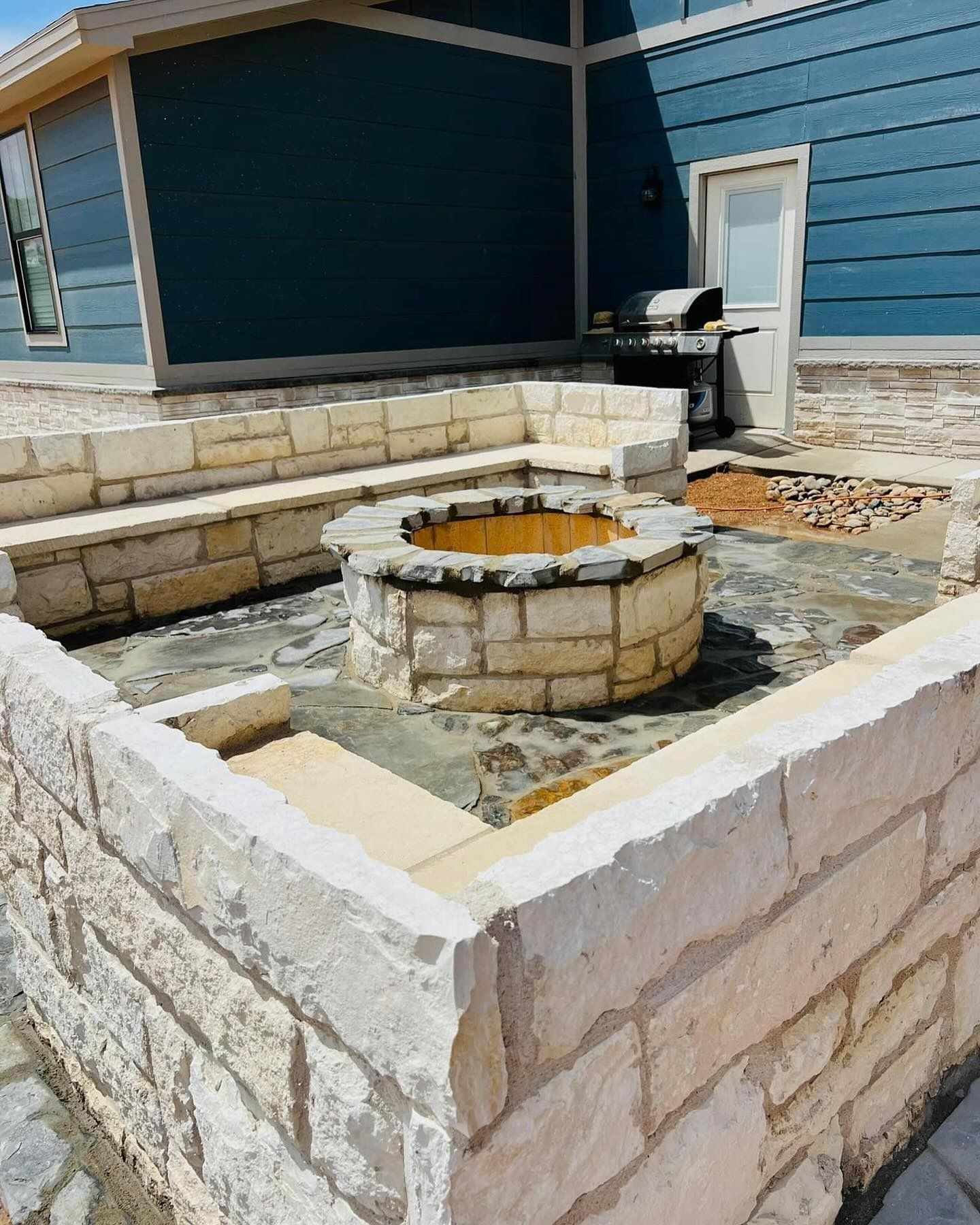 Stone fountain in a courtyard beside a blue house and black grill.