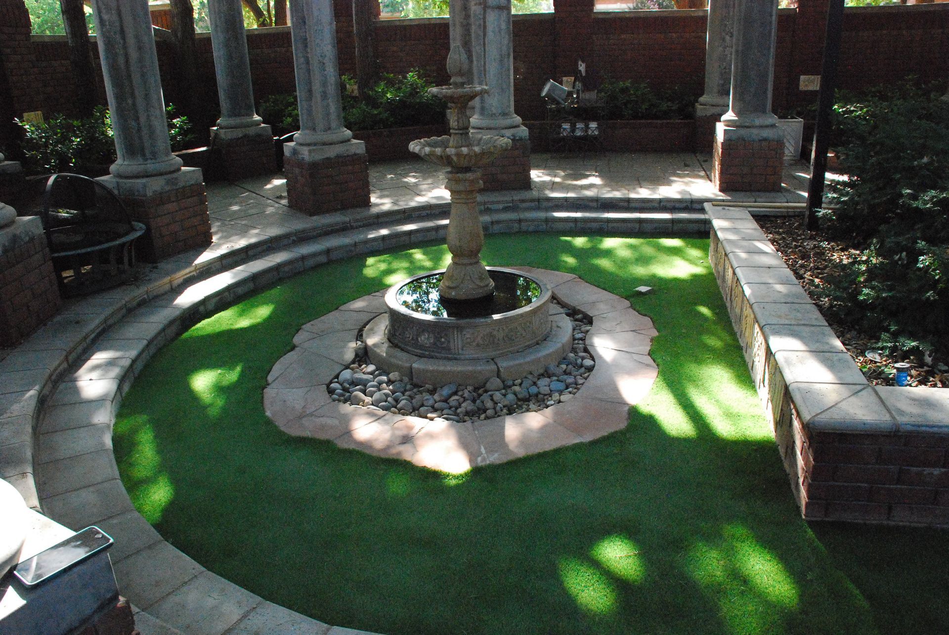Circular courtyard fountain with green water, stone border, and columns around it