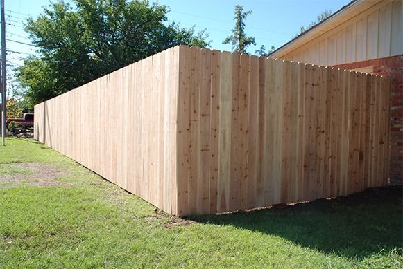 Long wooden privacy fence bordering a grassy yard beside a house.