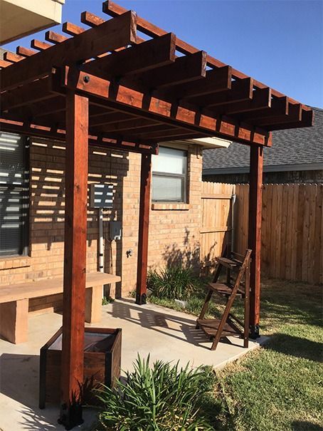 Wooden backyard pergola casting striped shadows beside a patio and fence in sunlight