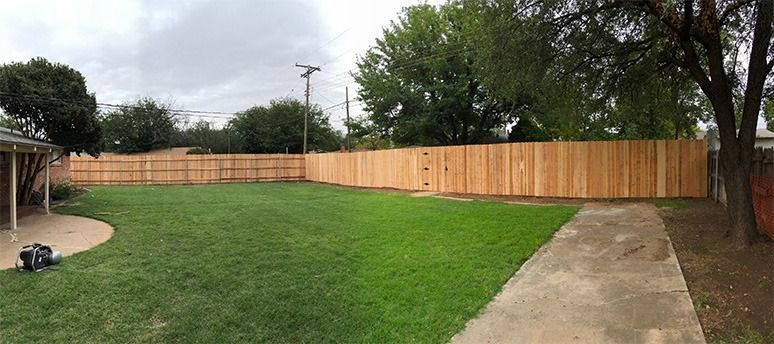 Backyard with green lawn, concrete walkway, and long wooden fence under cloudy sky