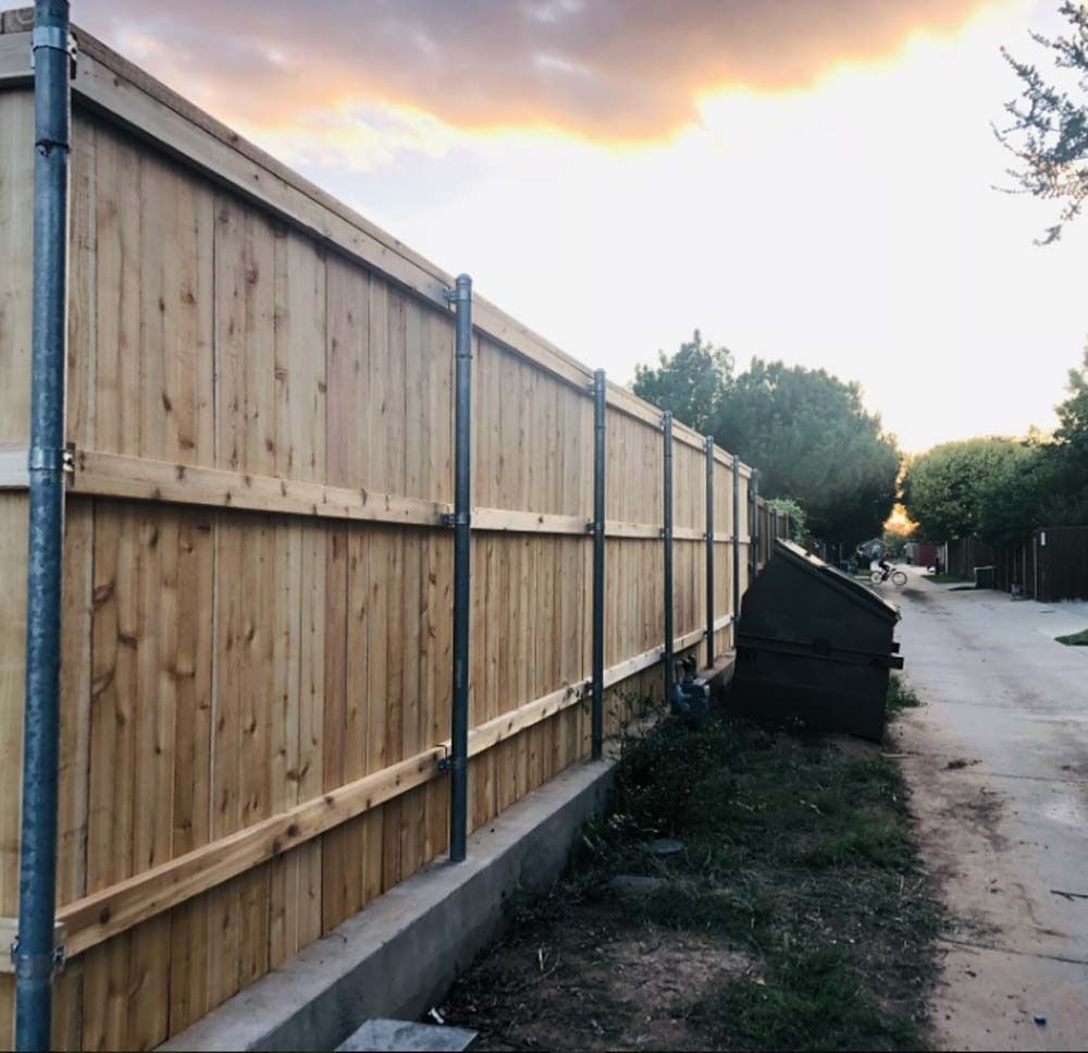 Wooden privacy fence along a narrow path at sunset, with trees and a quiet street beside it.