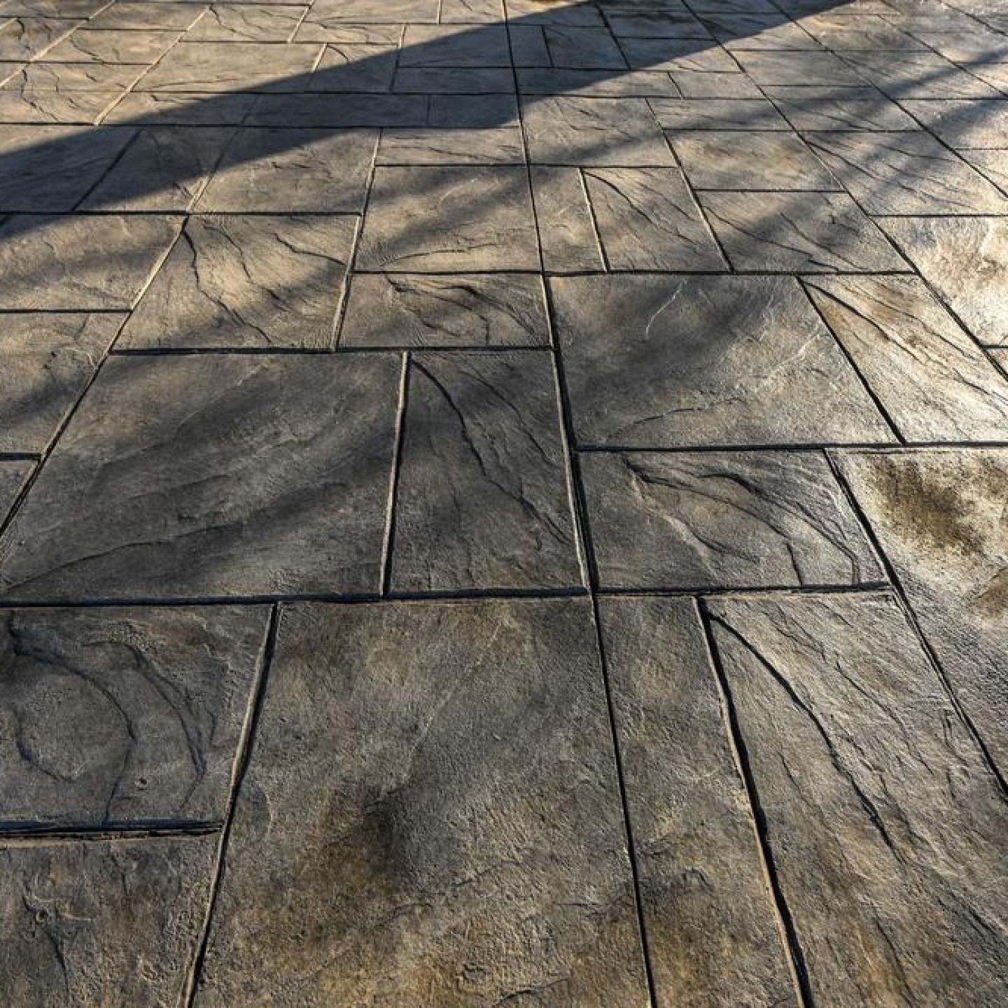 Patterned stone pavement with tree shadows across a sunlit ground