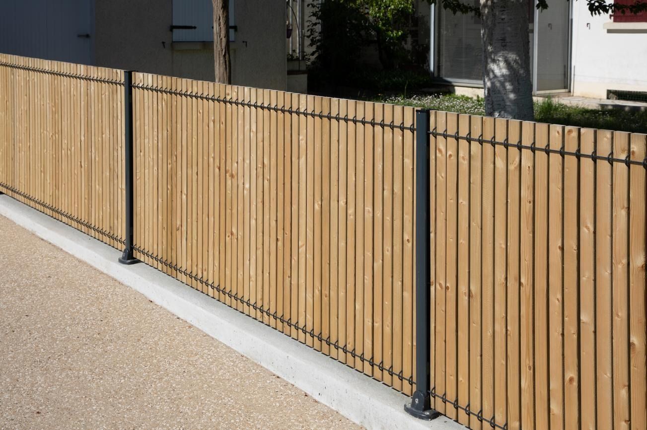 Wooden slat fence with black metal posts along a sidewalk and gravel path