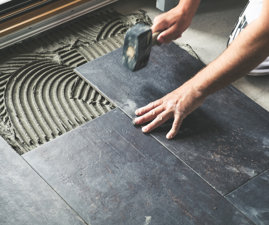 A man is laying tiles on the floor with a hammer.