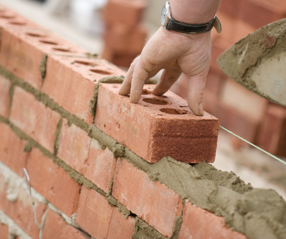 A person is laying bricks on a wall with a shovel.