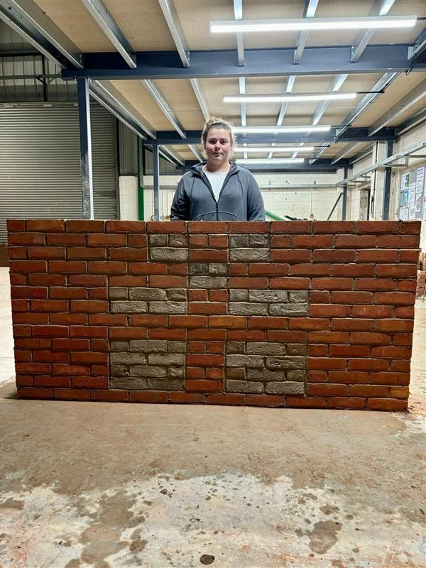 A man is standing in front of a large brick wall.