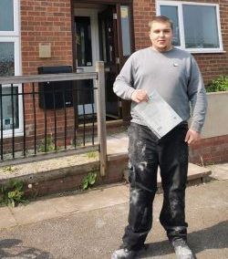 A man is standing in front of a brick house holding a piece of paper.