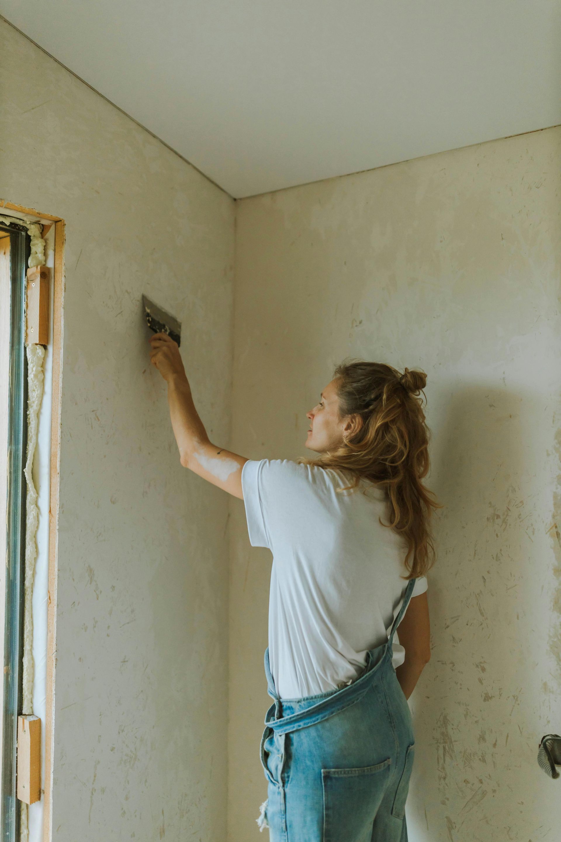 A woman is painting a wall with a spatula.