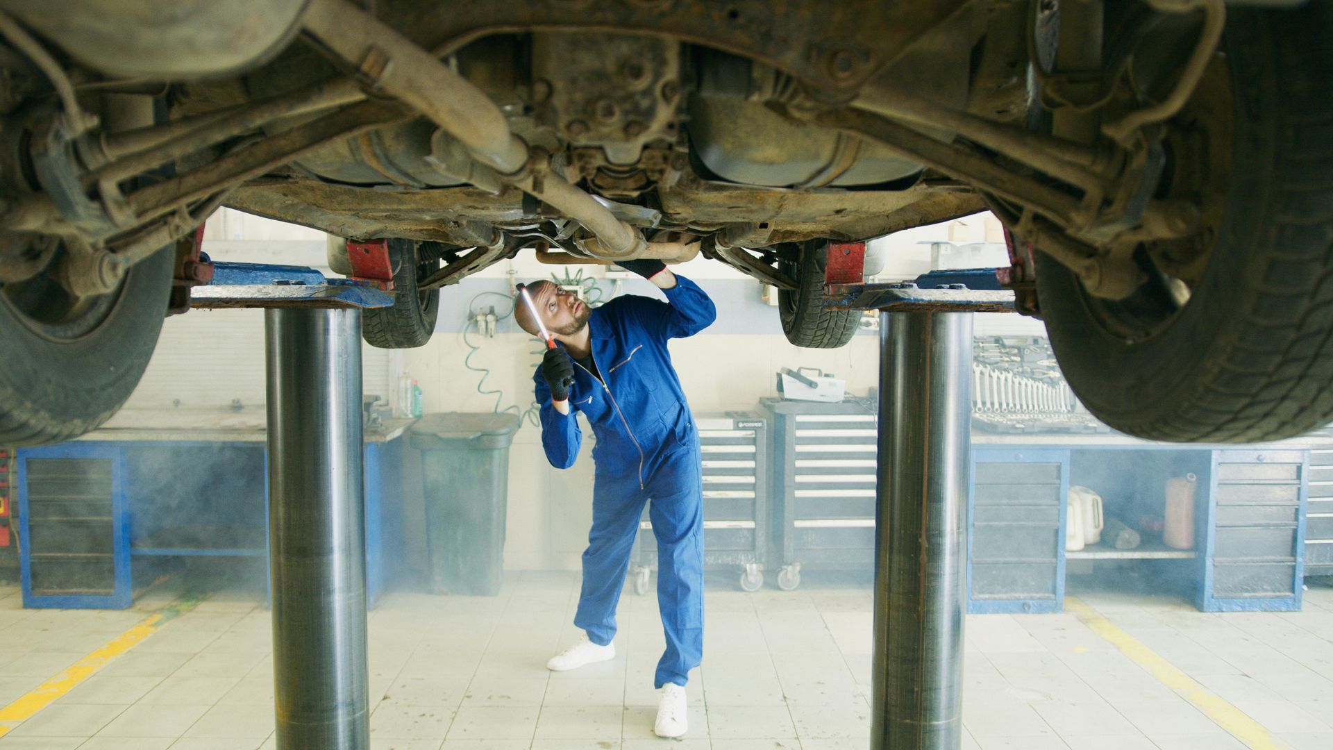 A mechanic is working under a car on a lift in a garage.
