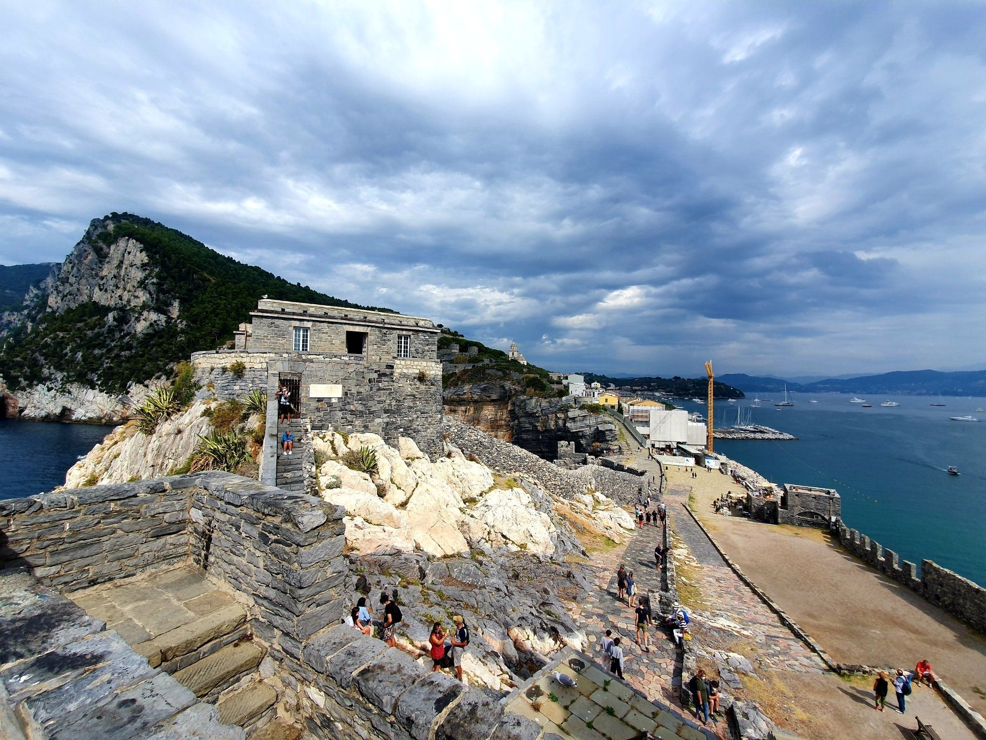 Middeleeuwse stenen vesting met uitzicht op zee onder een bewolkte hemel. Mensen lopen over de muur. Portovenere