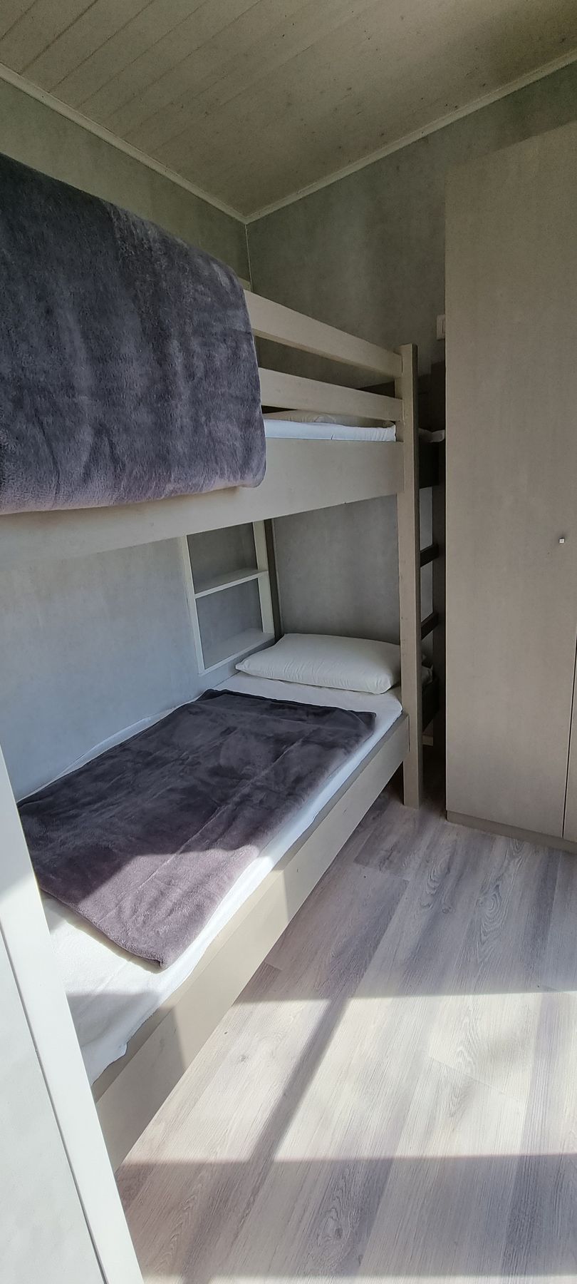 Stapelbedden in een kamer. Grijs-wit kleurenschema. Natuurlijk licht door een raam.