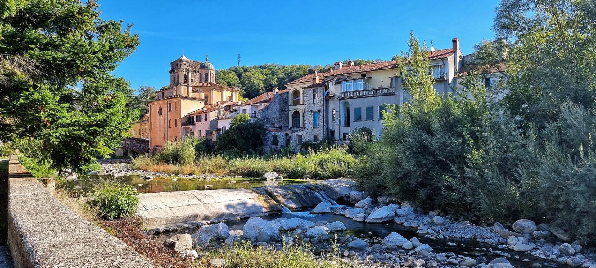 Gebouwen in een dorp aan een rivier onder een helderblauwe hemel. Pontremoli