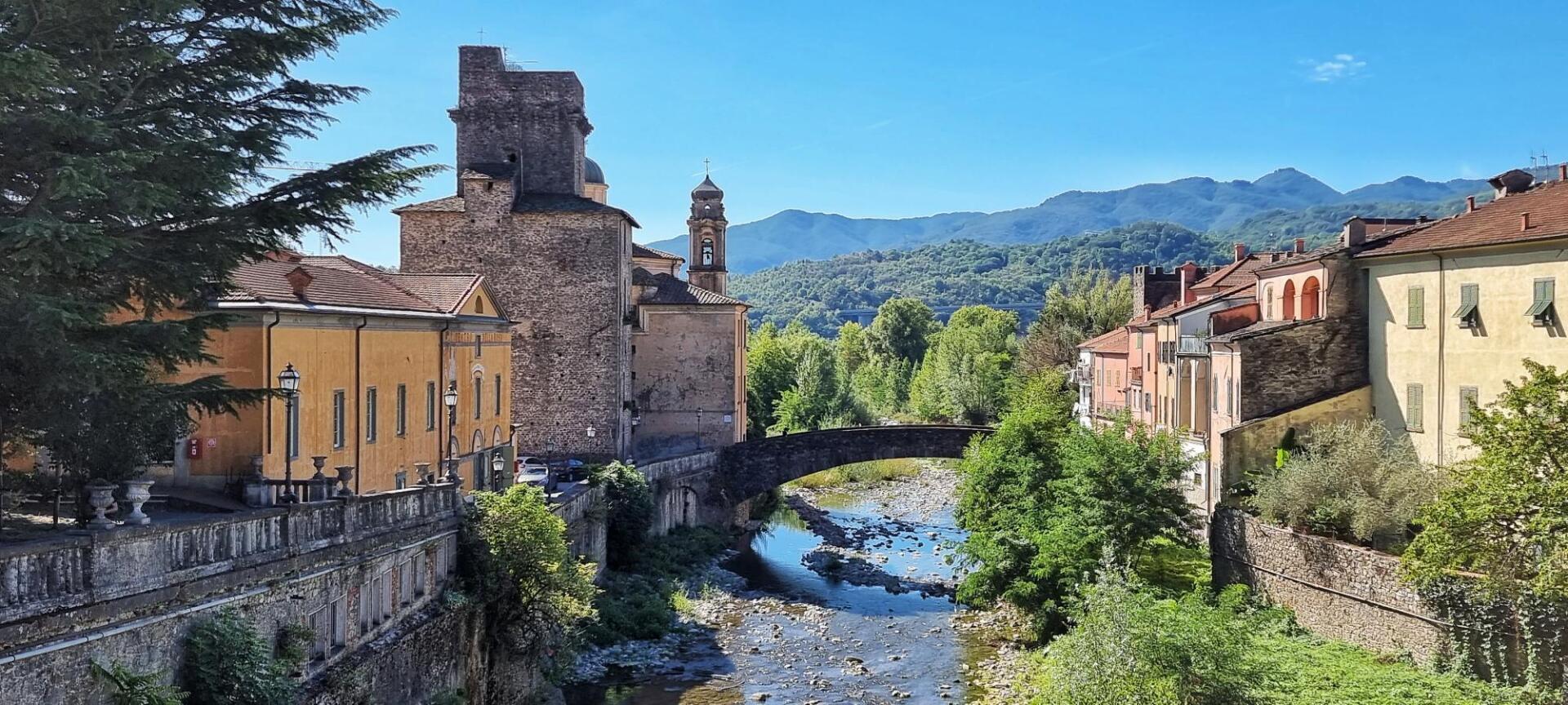 Langs een rivier met een stenen brug en bergen op de achtergrond staan stenen gebouwen. Pontremoli