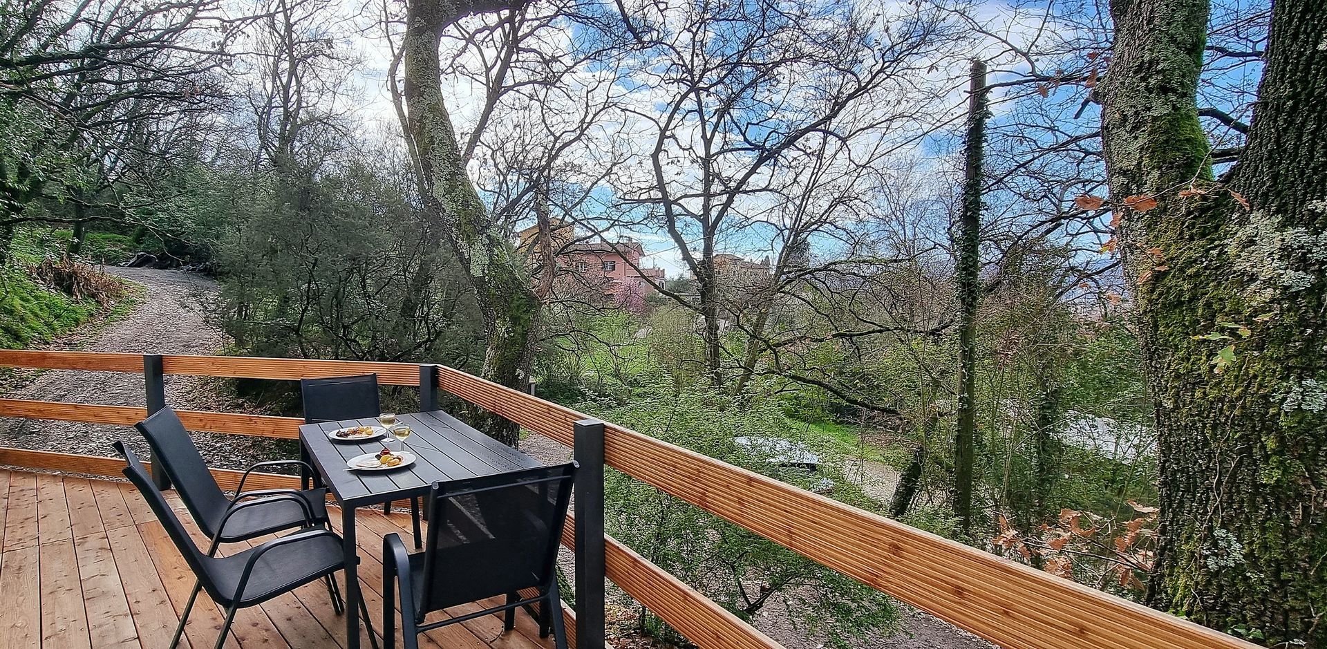 Een houten terras met een tafel en stoelen, met uitzicht op een bos. Het huis heeft schuifdeuren van glas.