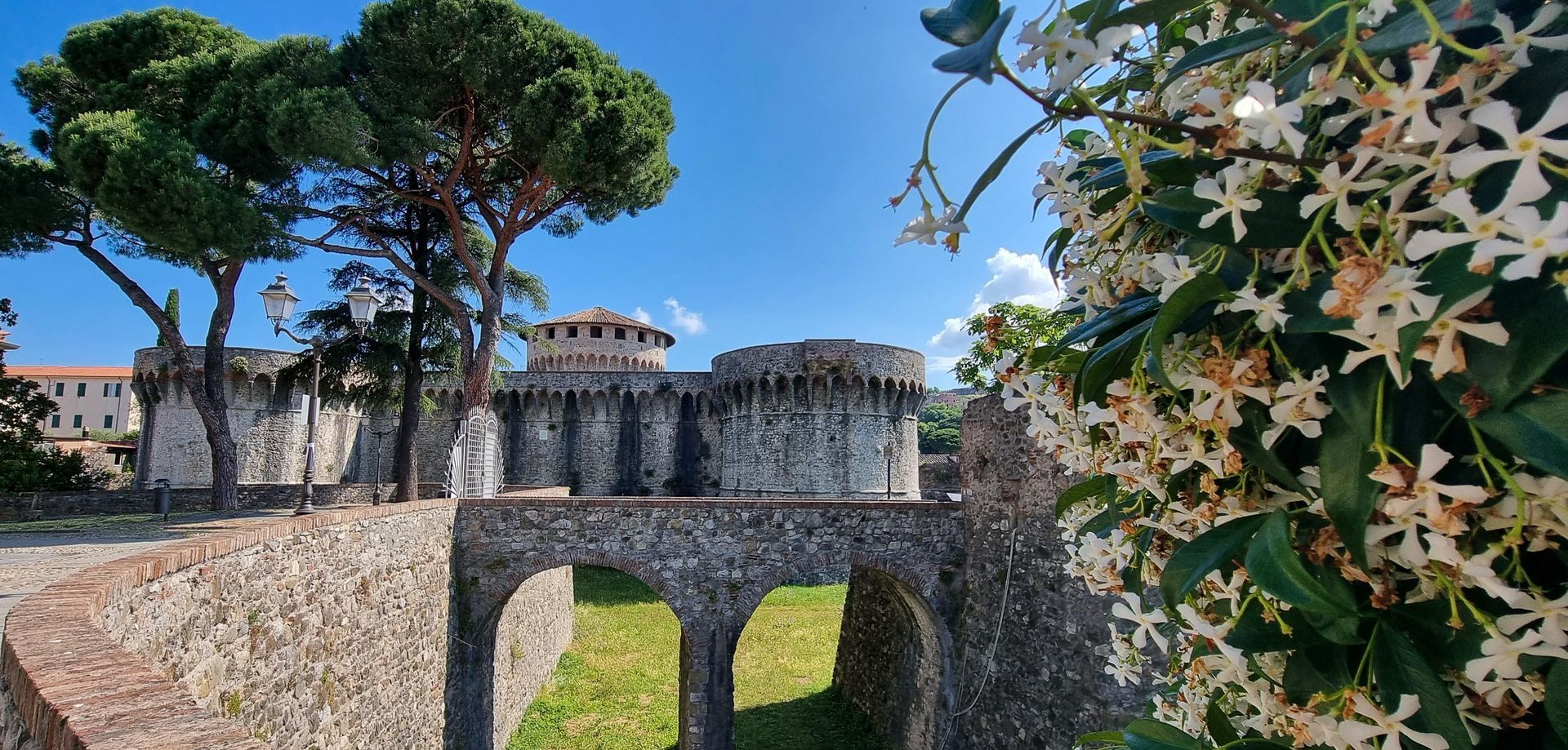 Stenen kasteel met een boogbrug over een groene gracht. Sarzana
