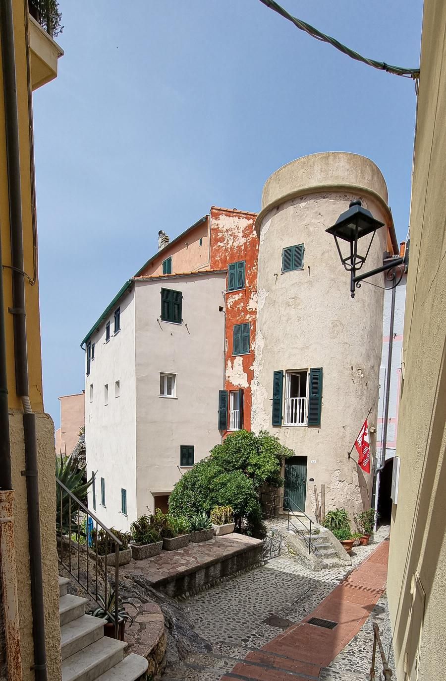 Witgekalkte gebouwen met groene luiken in een smalle Italiaanse straat, met een ronde toren.