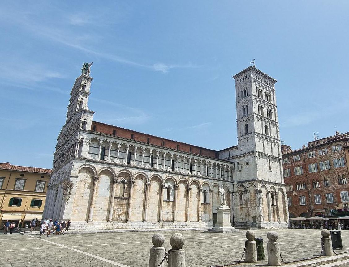De buitenkant van de kerk San Michele in Foro in Lucca, Italië. Witte stenen gevel, hoge klokkentoren, blauwe lucht.