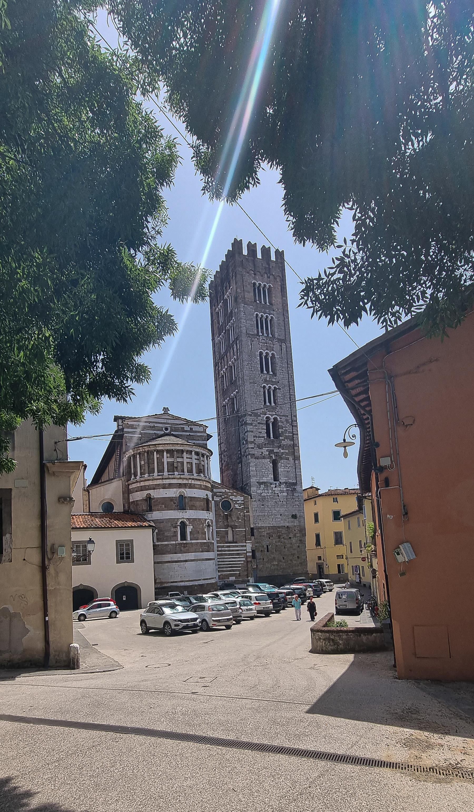 Uitzicht op Lucca, Italië, met de Guinigi-toren en omliggende gebouwen op een zonnig plein.